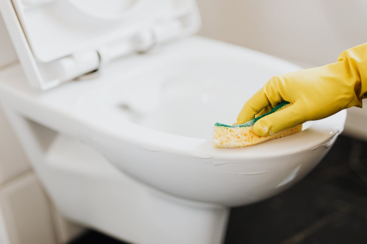 home-hero Close-up of a gloved hand using a sponge to clean a toilet, focusing on hygiene.