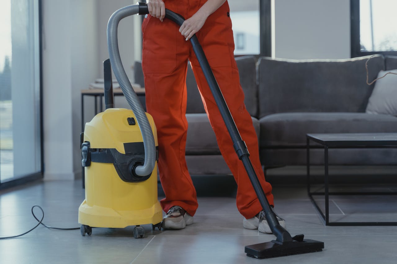 services-05 A professional cleaner in red coveralls vacuums a contemporary living room with a yellow vacuum cleaner.