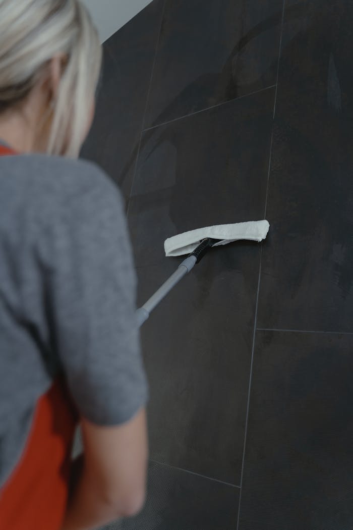 why-choose-us Close-up of a woman cleaning a dark wall with a mop, highlighting modern home cleaning methods.